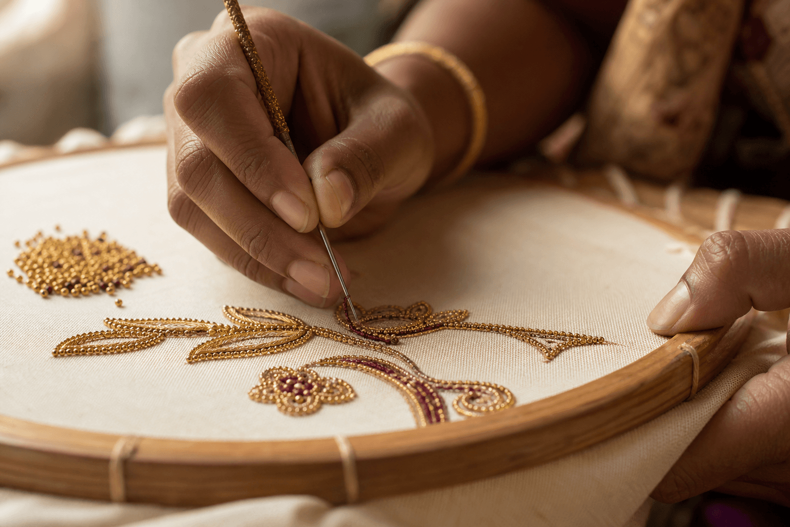 Artisan hands hand-embroidering a floral motif with gold Aari thread on a wooden frame